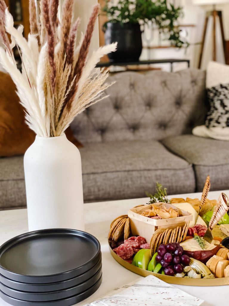 fall cheese board and black stoneware plates with pampas grass vase on a coffee table in a living room with a gray couch